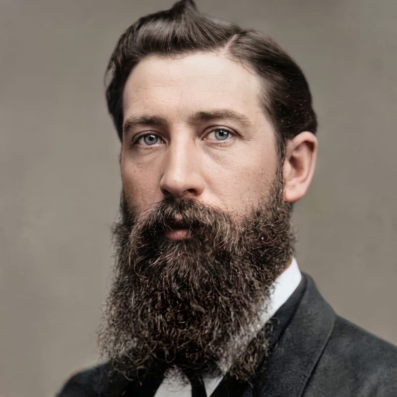 Restored and colorized formal portrait of a dark-haired man with a long beard, in a dark suit and tie