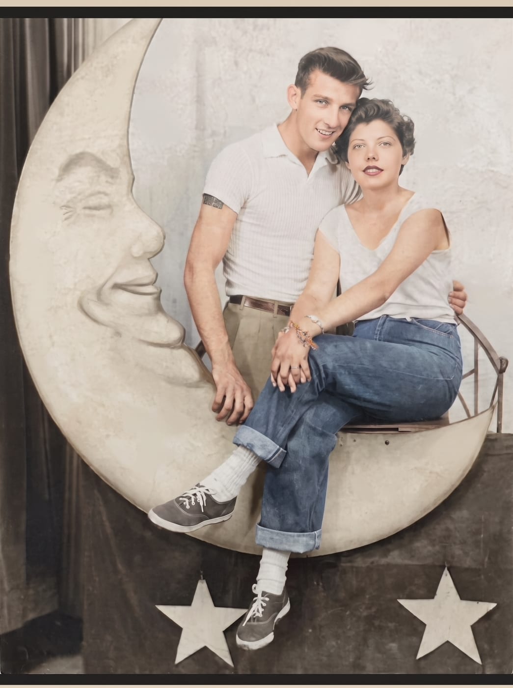 Restored and colorized fairground photograph of a young couple sitting on a crescent moon prop