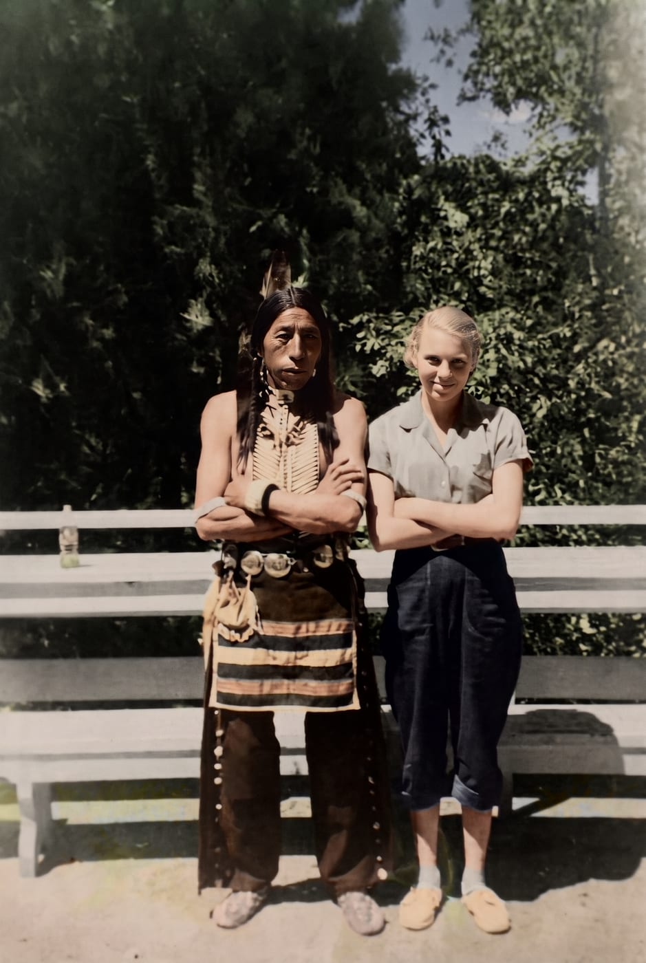 Restored and colorized photograph of two people standing arms folded in front of a park bench