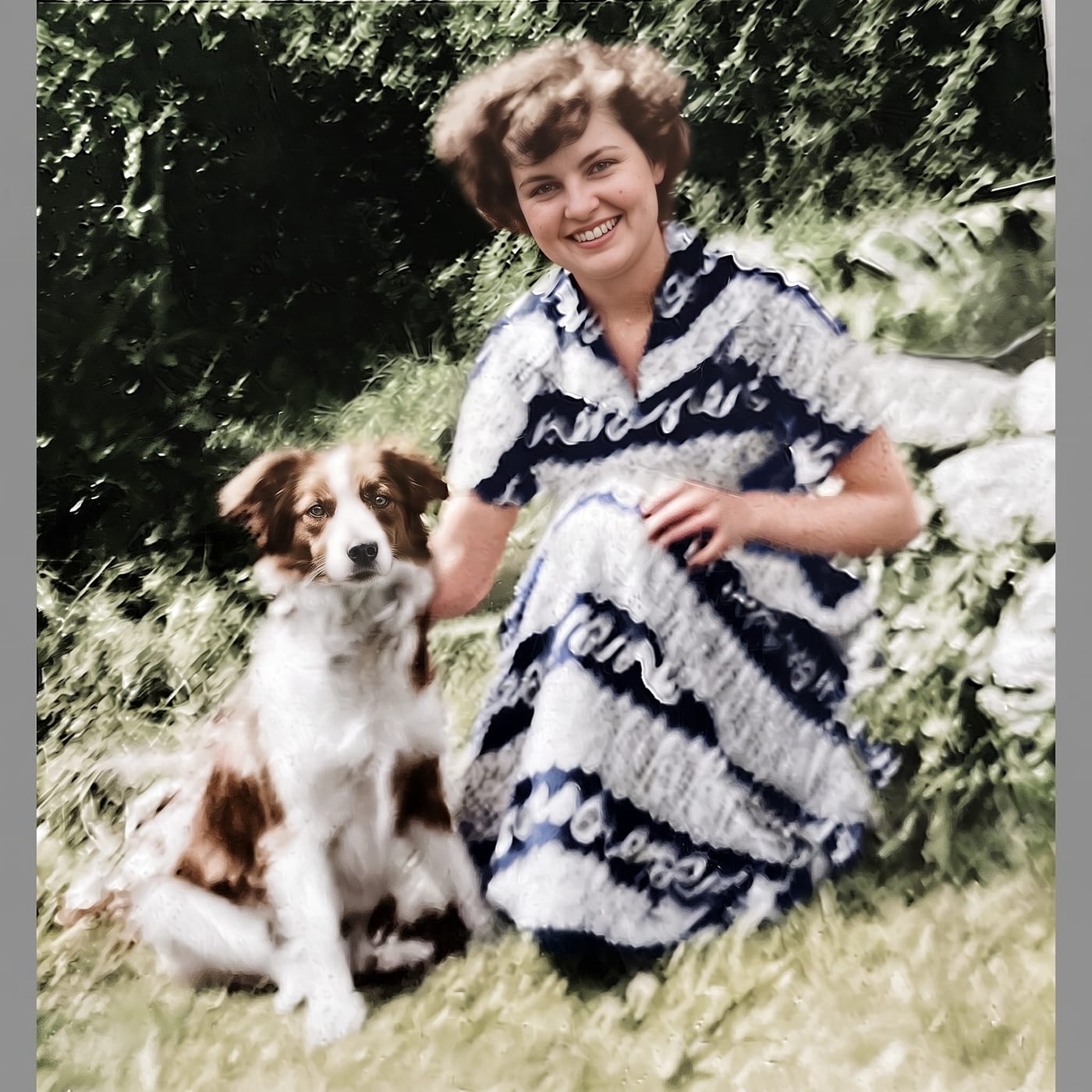 Restored and colorized photograph of a young woman in a banded dress sitting on the grass with her dog
